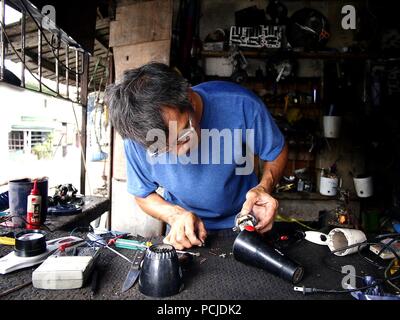 ANTIPOLO CITY, PHILIPPINES - AUGUST 1, 2018: A electrician fixes an electronic household item in his repair shop. Stock Photo