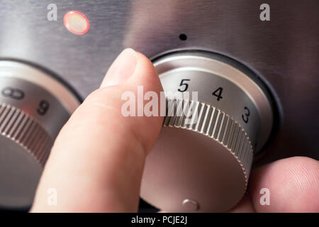 Male Hand Using Stove Controls To Set The Heat Level For A Hotplate, Set To 5 With Turned On Light Stock Photo