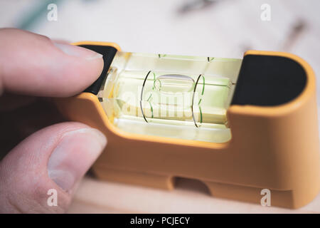 Male Fingers Holding A Small Yellow Spirit Level To Check If The Bubble Is In Center, DIY Home Improvement Concept Stock Photo