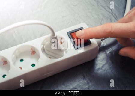Female Hand Pressing Red Switch Of Multiple Socket Outlet, Saving Energy Concept Stock Photo