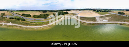 Panorama in high resolution, composed of photos with the drone, from the centre of a new rainwater retention basin to a new development and a country  Stock Photo