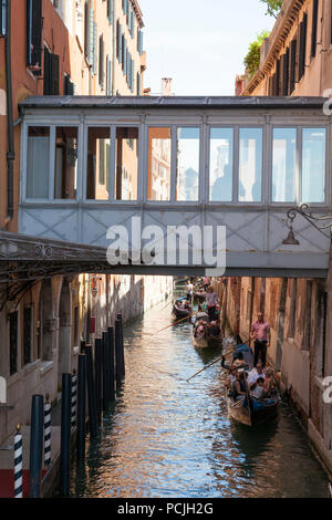 Gondolas with tourists  in a narrow canal Castello, Venice, Veneto, Italy passing under a covered skywalk between the Danieli Hotel palazzos Stock Photo