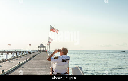 security guard sitting in a chair looking through binoculars on a pier in Montauk, NY Stock Photo