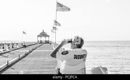 security guard sitting in a chair looking through binoculars on a pier in Montauk, NY Stock Photo