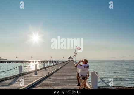 security guard sitting in a chair looking through binoculars on a pier in Montauk, NY Stock Photo