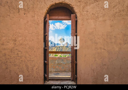 Narrow archway with old, heavy wooden doors opened to show the famous frankincense monument of Muscat, Oman. Stock Photo