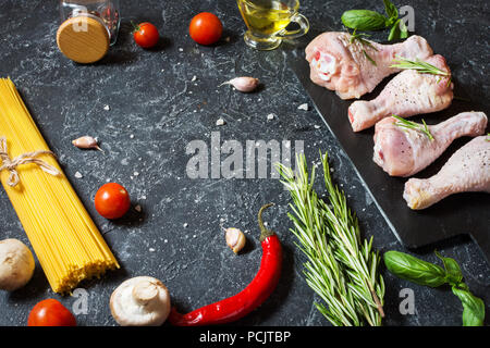 Pasta ingredients. Chicken legs drumsticks, Cherry tomatoes, spaghetti pasta and mushrooms on the stone table. Top view with space for text. Stock Photo