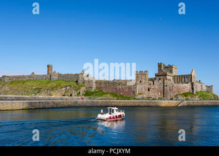 Peel castle ruins with boat heading out to sea from harbour. Peel, Isle of Man, British Isles Stock Photo