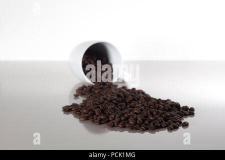 Pile of dark roasted coffee beans falling out of a white cup Stock Photo