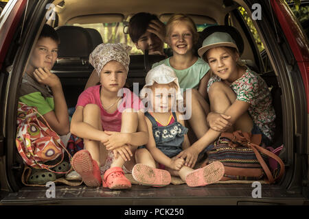 Group of smiling children big family in car trunk luggage going to road trip in family car symbolizing kids friendship and happy carefree childhood Stock Photo