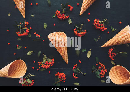Waffle ice cream cone flat lay top view on dark black wooden background decorated with wild berry fruit arrangement Stock Photo