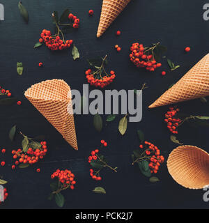 Waffle ice cream cone flat lay top view on dark black wooden background decorated with wild berry fruit arrangement Stock Photo