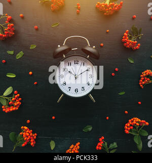 Ten past ten on alarm clock, flat lay top view minimal composition of timepiece placed on dark wooden background with retro floral arrangement Stock Photo