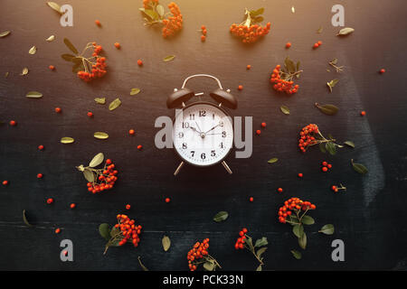 Ten past ten on alarm clock, flat lay top view minimal composition of timepiece placed on dark wooden background with retro floral arrangement Stock Photo