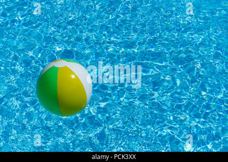 Inflatable multicolored ball floating on swimming pool water, with copy space, summer recreation concept. Stock Photo