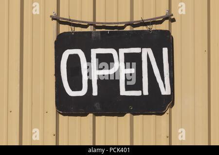 Open signboard with white painted letters on a black weathered board against a yellow wall. Stock Photo