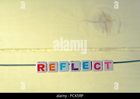 A Studio Photograph of Alphabetical Beads Suspended on a Wire Spelling 'Reflect' Stock Photo