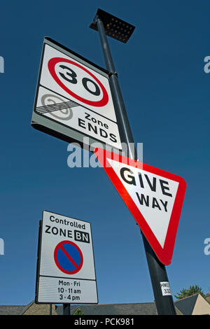 british road signs indicating give way, the start of a 30mph speed limit and the end of a 20mph speed limit zone, with controlled parking sign to rear Stock Photo