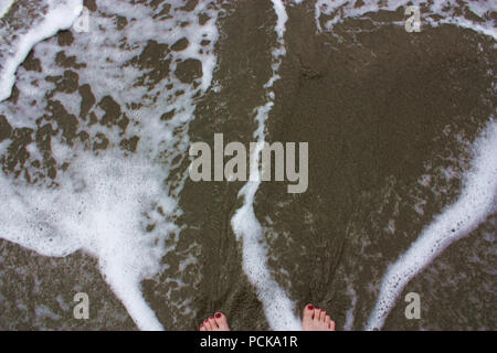 Woman's feet with red toenail polish in foamy, shallow water on a beach in Hawaii, USA Stock Photo