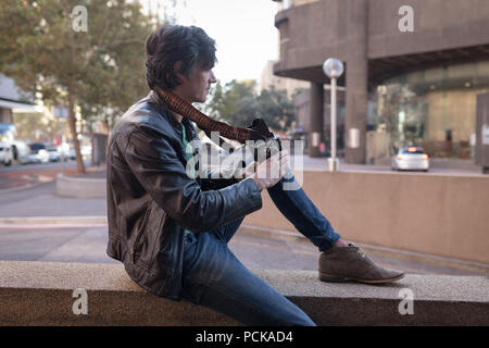 Photographer with camera sitting on surrounding wall Stock Photo