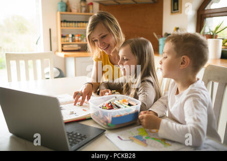 Mother helping children with homework in kitchen Stock Photo
