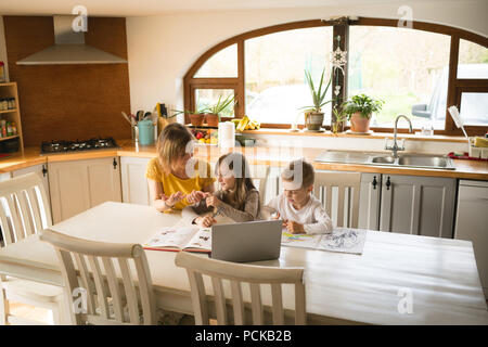 Mother helping children with homework in kitchen Stock Photo