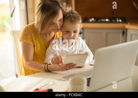 Mother with son sitting on chair using digital tablet in kitchen Stock Photo