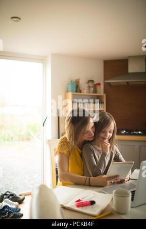 Mother with daughter sitting on chair using digital tablet in kitchen Stock Photo
