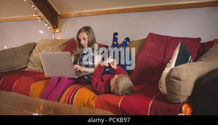 Sibling using multimedia devices on sofa Stock Photo