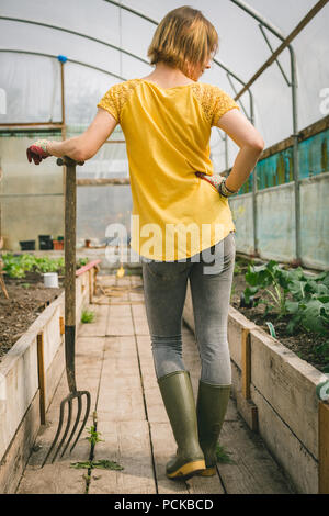 Woman with digging fork standing in greenhouse Stock Photo