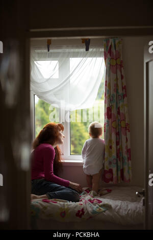 Mother with her baby girl looking through window Stock Photo