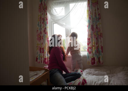 Mother with her baby girl looking through window Stock Photo