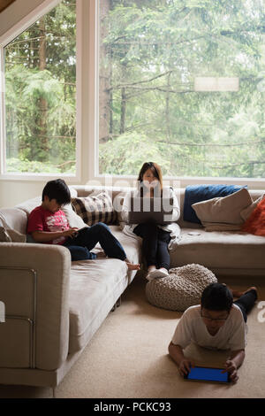 Mother using laptop while kids using digital tablet in living room Stock Photo