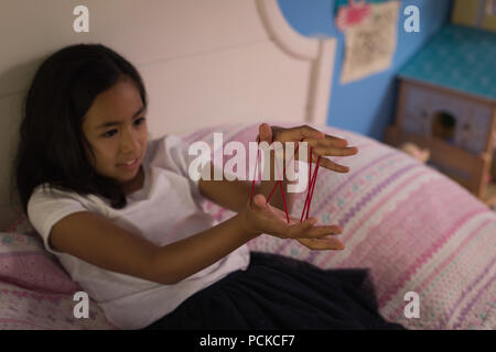Girl playing cats cradle game in bedroom Stock Photo