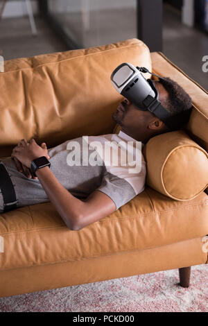 Man experiencing VR headset while lying on sofa Stock Photo