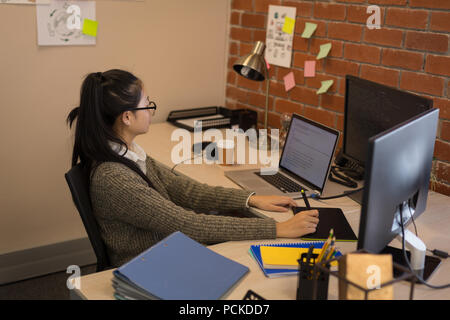 Female graphic designer using graphics tablet at desk Stock Photo