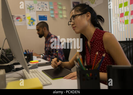 Female graphic designer using graphics tablet at desk Stock Photo