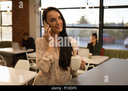 Female executive talking on mobile phone in cafeteria Stock Photo