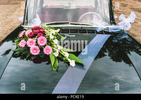 Vintage black car decorated with bouqet bunch of flowers and white ribbon for wedding, France. Stock Photo