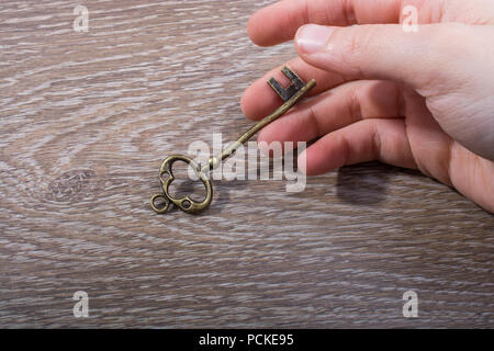 Hand holding a retro styled decorative key on wooden texture Stock Photo