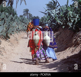 Tunisian Arab Berber women on their way to the Tozeur oasis to collect water in their amphora clay vessels Stock Photo