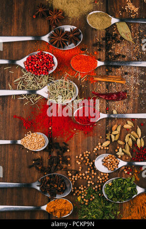 Top view of wooden table full of spices in spoons, you can see the most popular condiments and seasoners Stock Photo