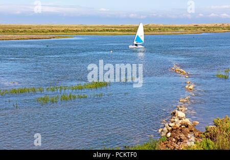 A solo yachtsman inbound at high water in a sailing dinghy in Overy Creek at Burnham Overy Staithe, Norfolk, England, United Kingdom, Europe. Stock Photo