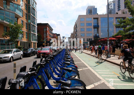 People dock CitiBike bicycles as cyclists pass on an adjacent bike lane next to Smorgasburg in Williamsburg, Brooklyn on JULY 8th, 2017 in New York, U Stock Photo