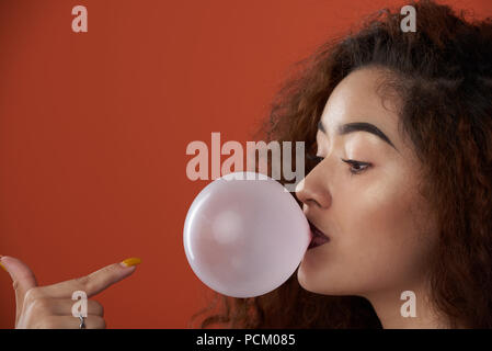 Young woman blow bubble gum blow portrait isolated on orange color background Stock Photo