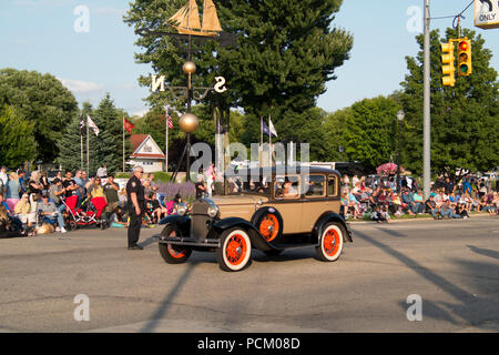 Antique Ford sedan rolls in the 2018 Annual Cruz-In parade through downtown Montague, Michigan. The world's largest operating weather vane sits in a c Stock Photo