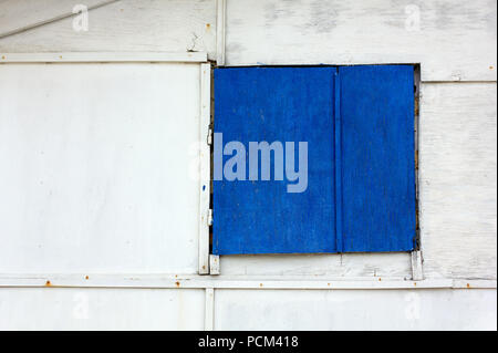 Closed window shutter painted in blue on a wooden exterior white wall Stock Photo