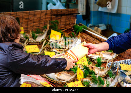 Kuromon Ichiba, Osaka's kitchen food market. Fish mongers. Hand handing over paper wrapped lobster to woman customer across counter with sea beams on. Stock Photo