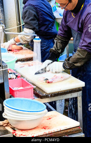 Kuromon Ichiba, Osaka's kitchen food market. Two men, standing while slicing fish up, working on table with running water flowing off the end. Stock Photo