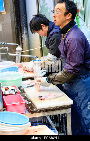 Kuromon Ichiba, Osaka's kitchen food market. Two men, standing while slicing fish up, working on table with running water flowing off the end. Stock Photo